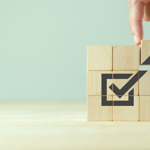 Eine Hand, die einen Würfel zusammenbaut, auf dem ein Häkchen abgebildet ist