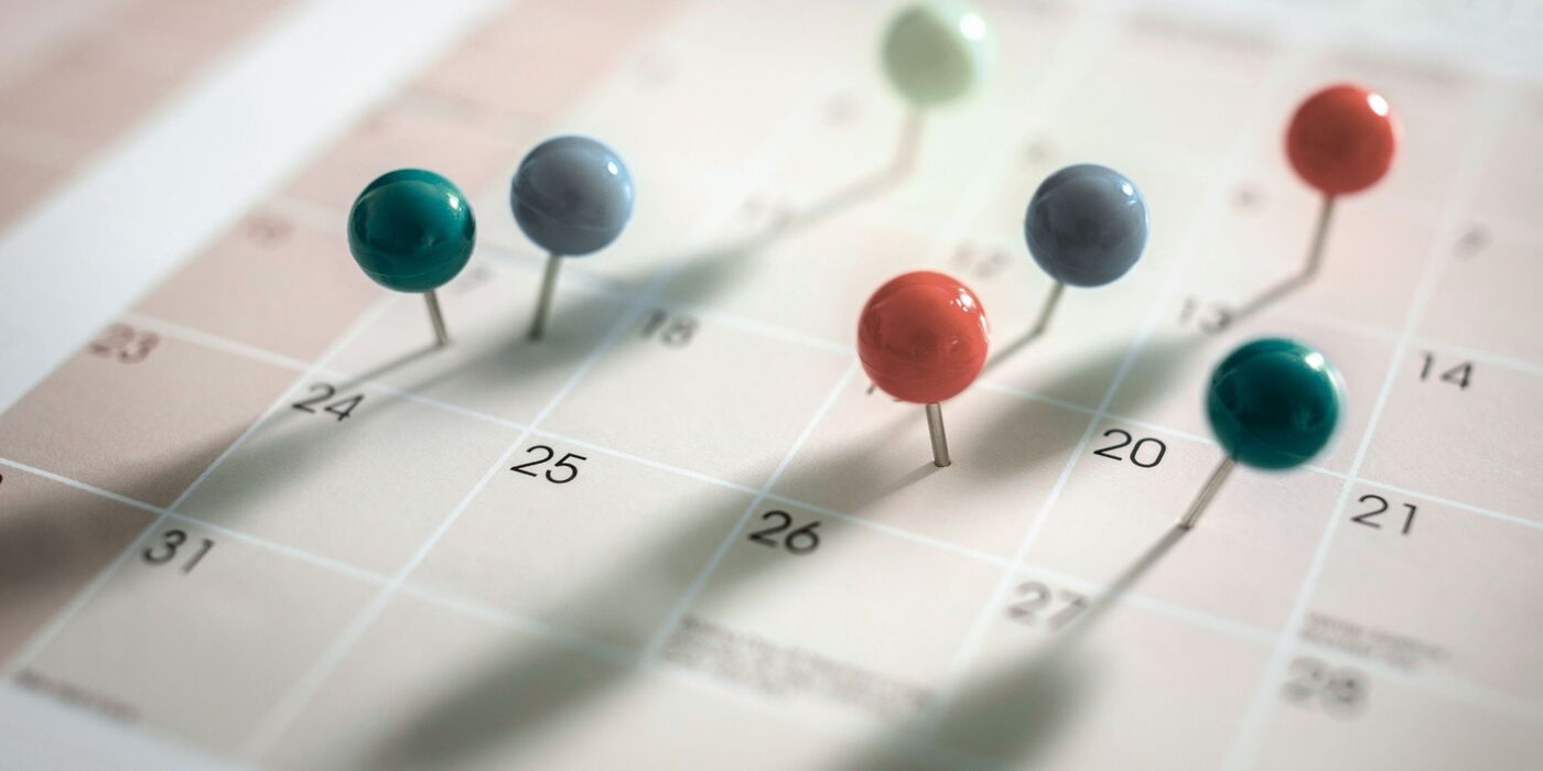 Mehrere bunte Stecknadeln markieren verschiedene Tage auf einem Kalenderblatt.
