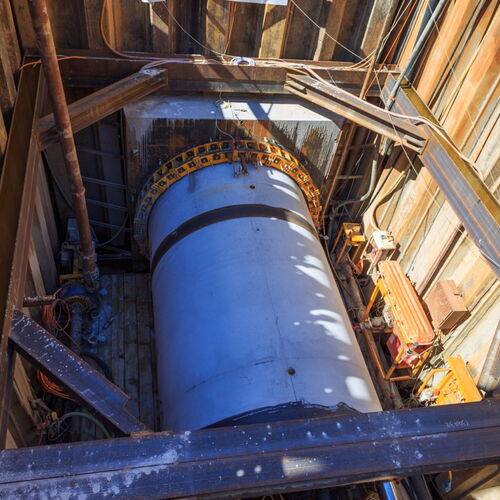Blick von oben auf eine Baustelle für Microtunneling: Ein großer, runder Tunnelbohrkopf befindet sich in einer mit Stahlwänden ausgekleideten Startgrube.