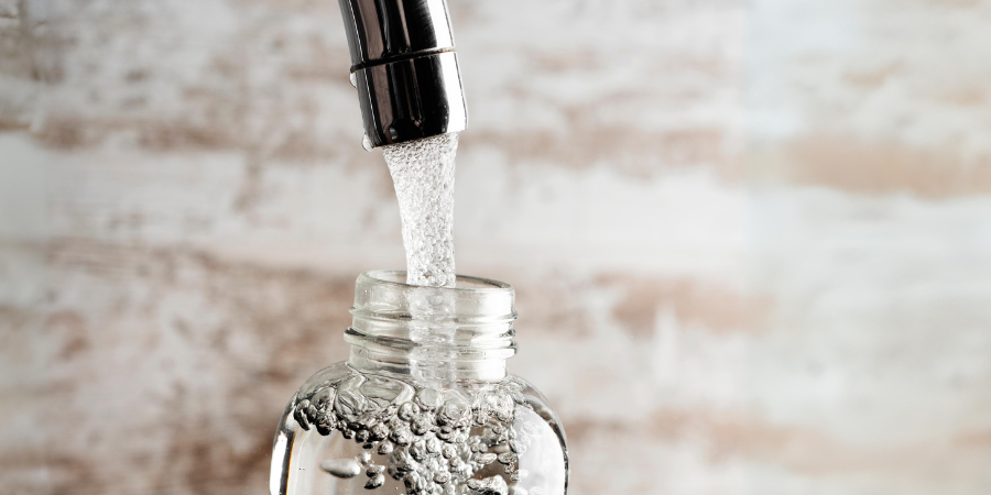 Flasche, in die Wasser aus einem Wasserhahn gefüllt wird.