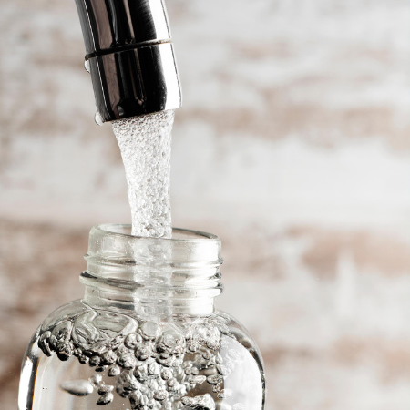 Flasche, in die Wasser aus einem Wasserhahn gefüllt wird.